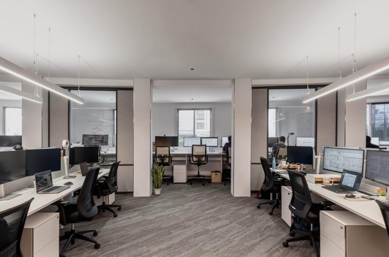 Grey Image of an office with multiple desk and chair.